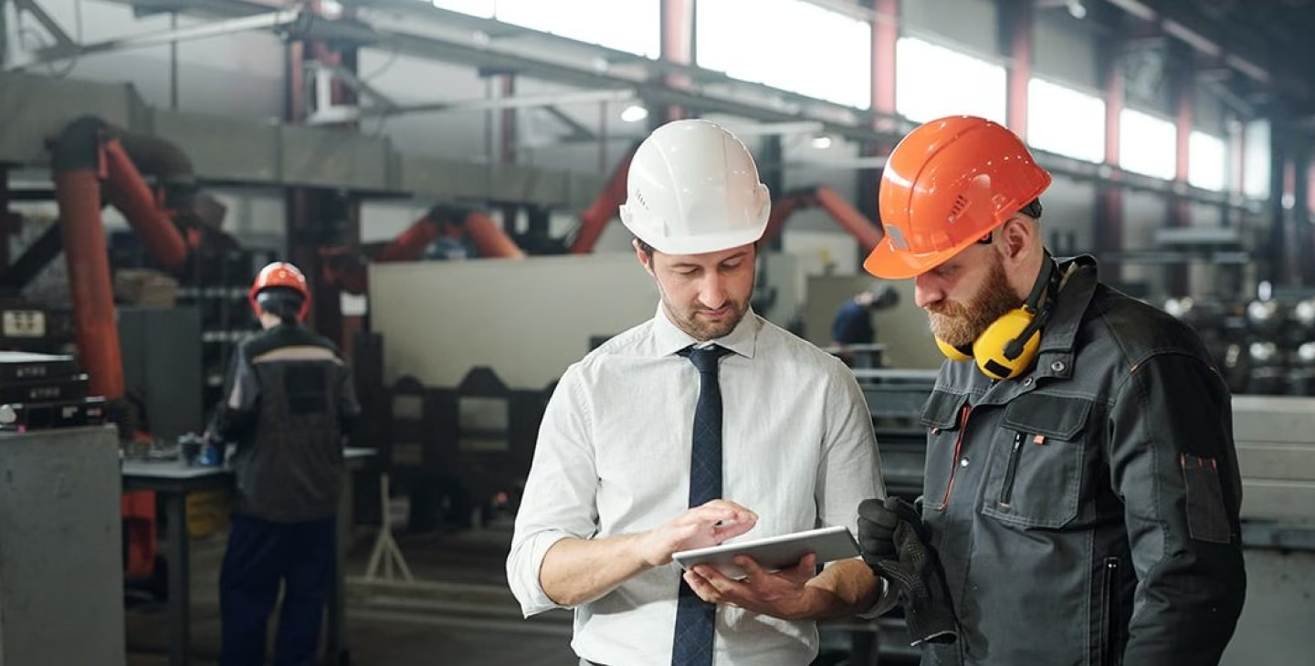Responsable en chemise et ingénieur en tenue de sécurité consultant des données sur tablette dans une usine de production.