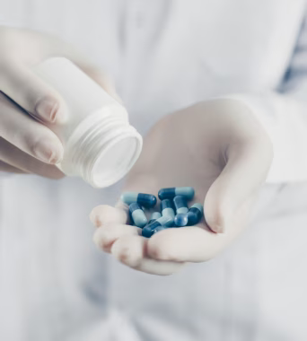 Gélules bleues versées dans la main d’un professionnel de santé