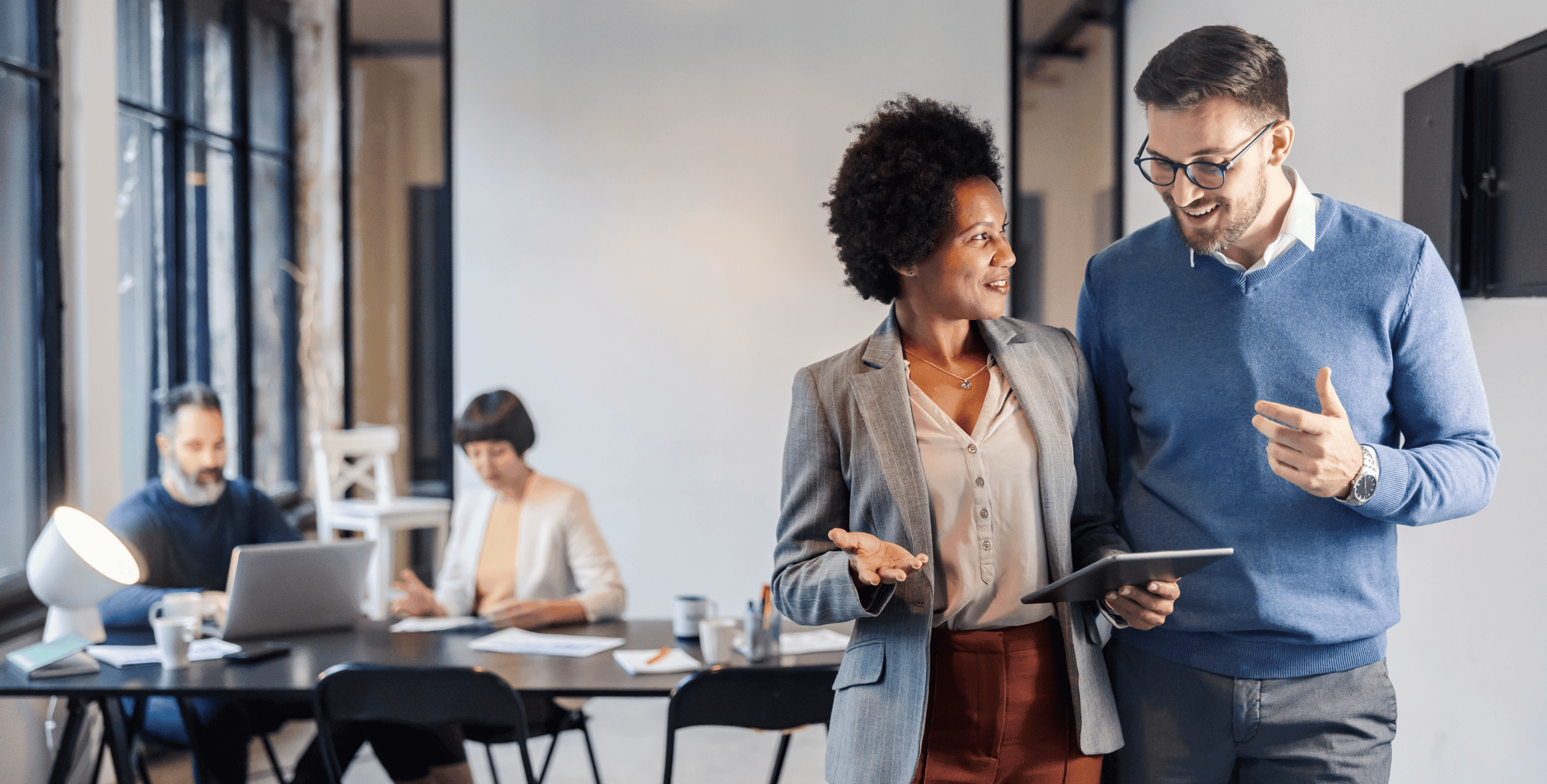 Deux collègues professionnels discutant et travaillant ensemble dans un bureau moderne avec des ordinateurs en arrière-plan